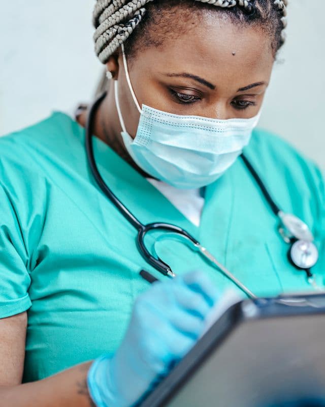 Nurse in scrubs and mask writing a care plan on a clipboard