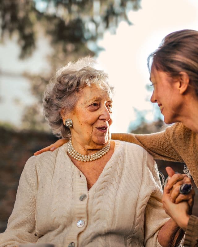Younger supporter holding hands with an older person during a care review outdoors