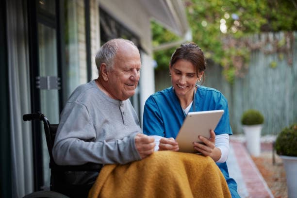 A nurse and a senior man in a wheelchair using a digital tablet together on a patio